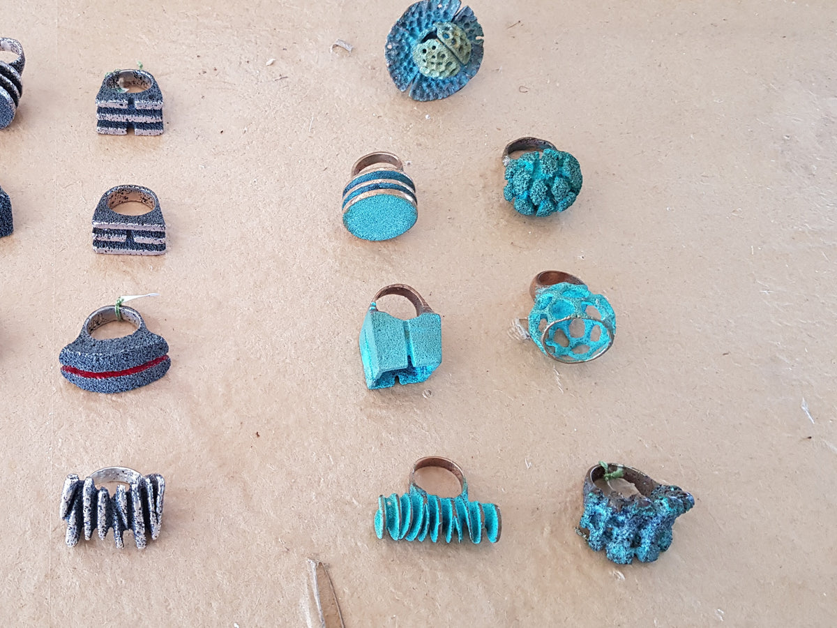 Rings finished with black and turquoise patina, laid out on a workbench